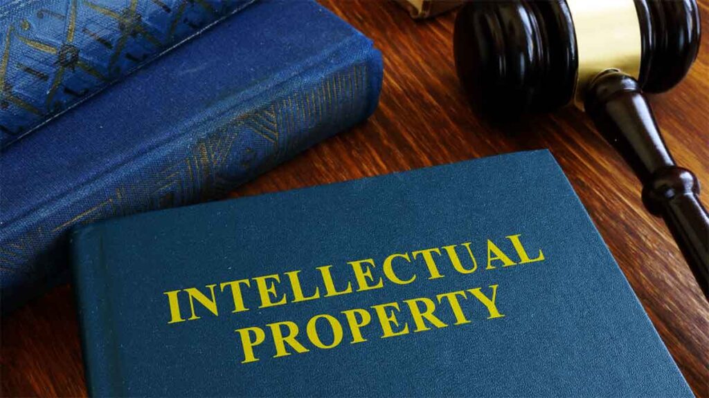 A book titled _Intellectual Property_ lies on a wooden table next to a gavel and another book