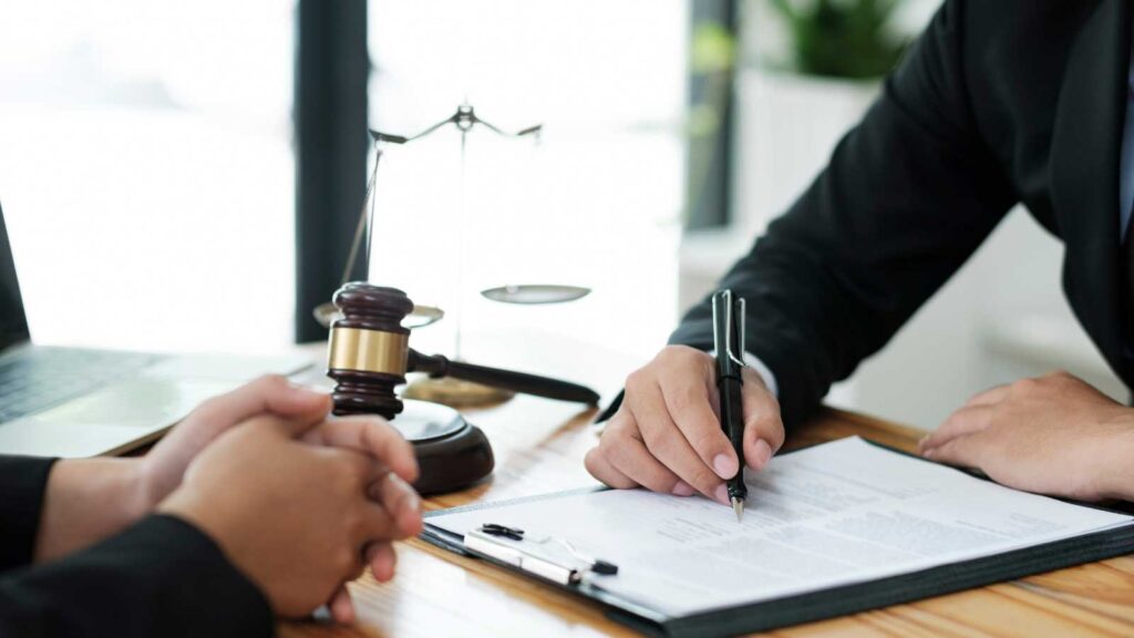 A person signing a document with a gavel and scales of justice on the table