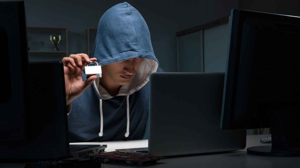 Man in hoodie suspected of brand identity theft using multiple computer screens.