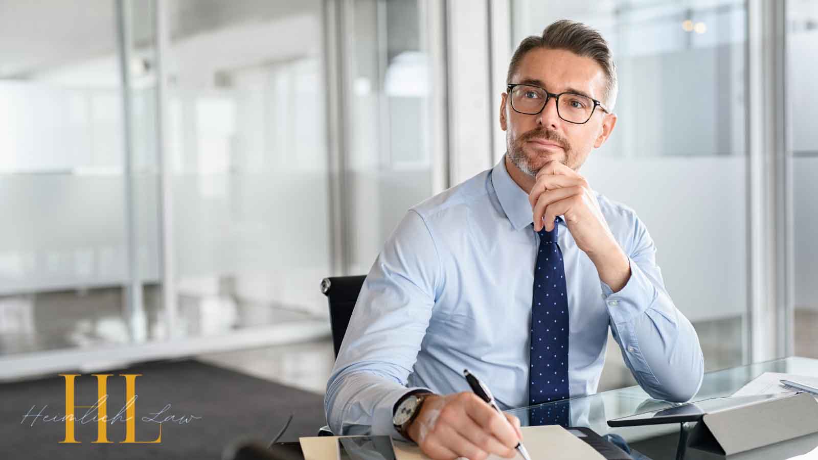 Man sitting at a desk, looking thoughtful with hand on chin