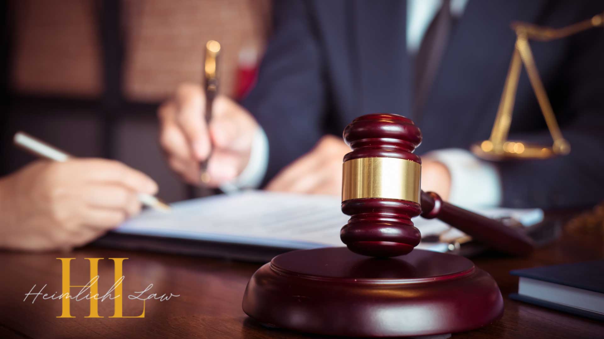 Two people sitting across a desk in a law office, with a gavel and scales of justice placed on the table.